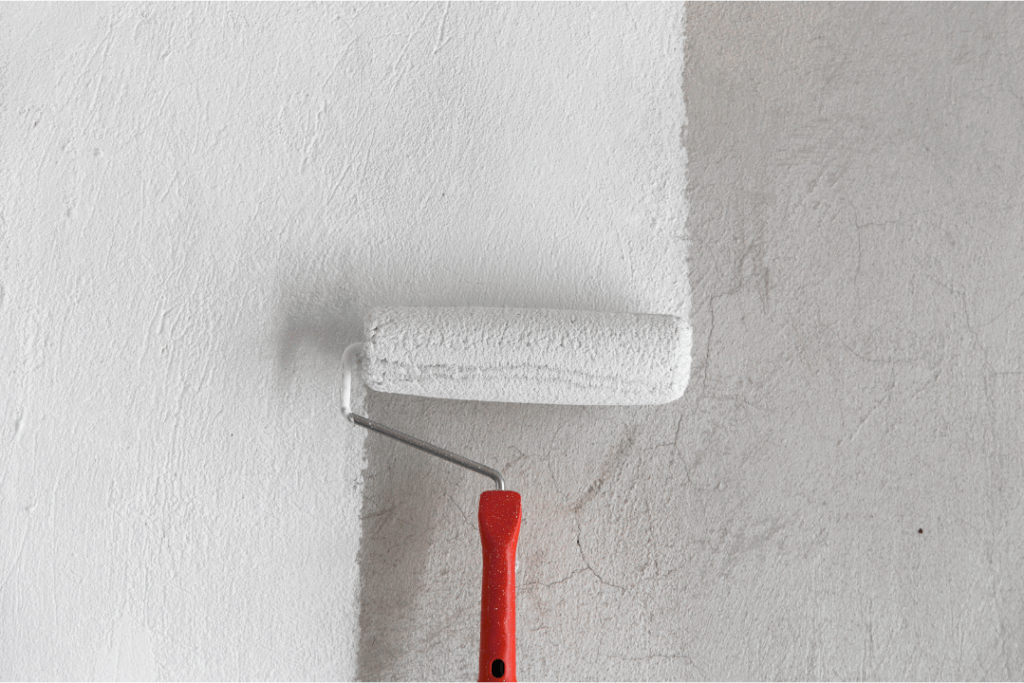 Paint roller applying white paint to a textured wall