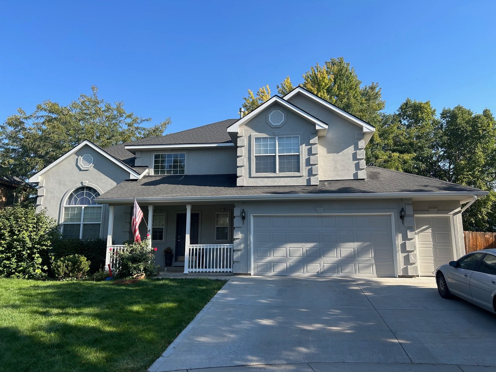 Two-story gray house with an American flag, manicured lawn, and clear blue sky, illustrating ideal painting conditions for homeowners.