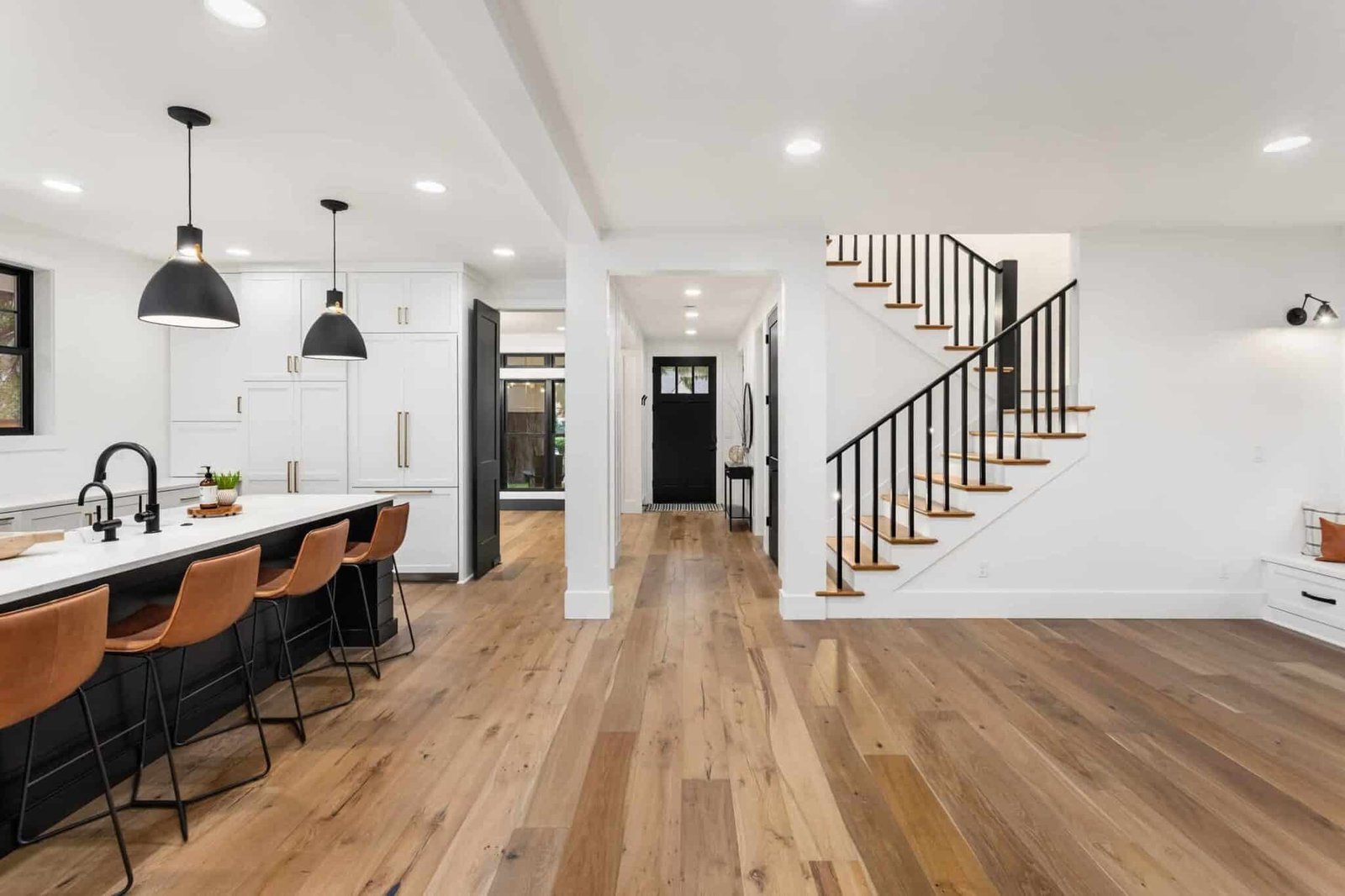 Open kitchen and living area with white walls, black pendant lights and wood floors