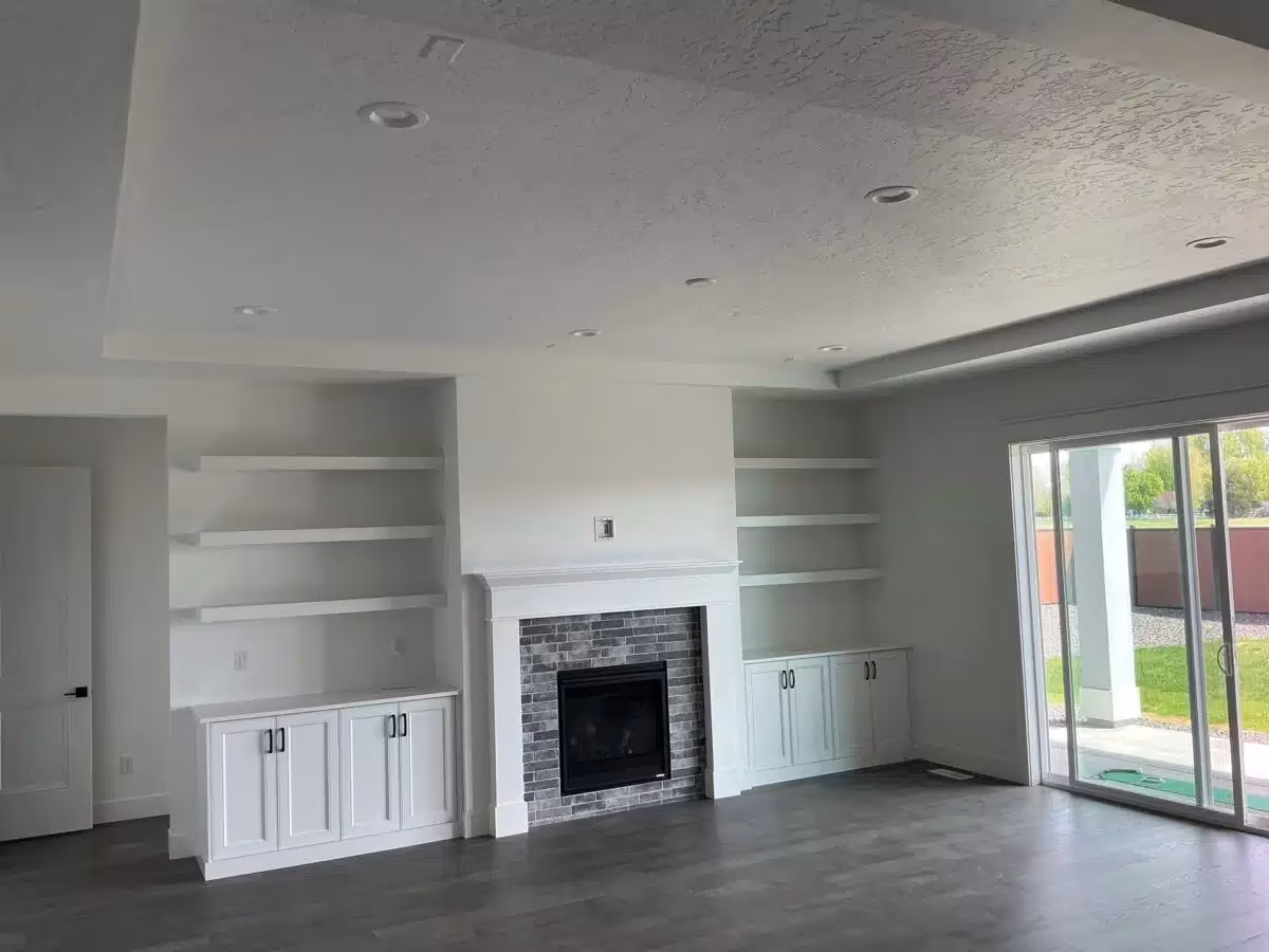 Modern living room interior with white walls, built-in shelving, a gray brick fireplace, and large sliding glass doors leading to an outdoor space, showcasing a clean and stylish design suitable for residential interior painting services.