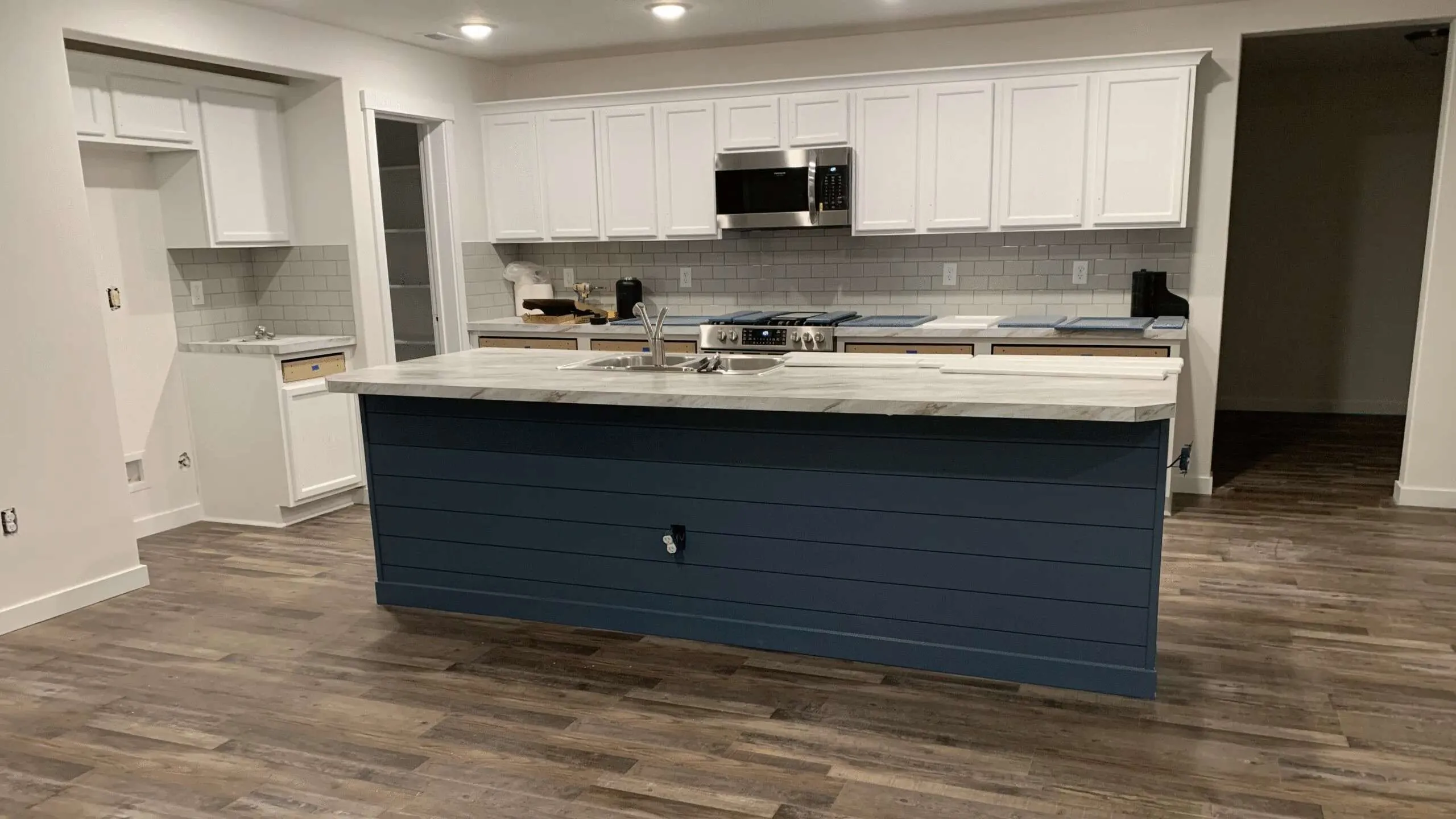 Kitchen cabinet refinishing in progress, with white cabinets and a navy shiplap island